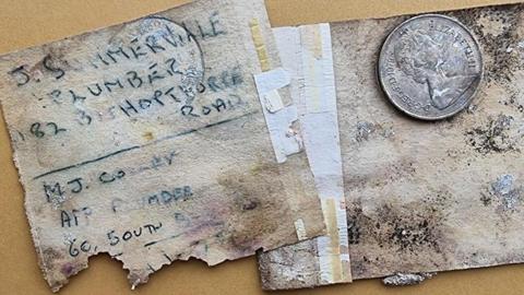 A 10p coin on a piece of paper, next to a note with torn edges. Faded pen writing on the note reads: "J. Summerville, plumber, 182 Bishopthorpe Road."