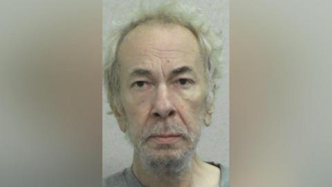 Mugshot of Southern. He is very pale and gaunt with straggly white receding hair and an unkempt white beard.