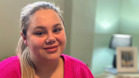 A young woman with blonde hair smiles at the camera