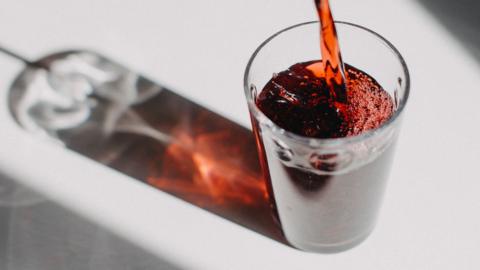 Cranberry juice is poured into a glass on a white background.