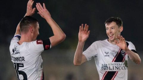 Lincoln goalscorer Conor McGrandles is congratulated for scoring at Chesham United by team-mate Paudie O'Connor 