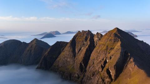 An Teallach in the Highlands. There is a ridge of five main peaks in a row. The ridge and mountains behind are rising out of low cloud which has been captured by a temperature inversion.