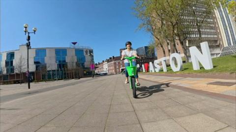 A woman wearing a white top and jeans riding a green and white cycle on a piazza