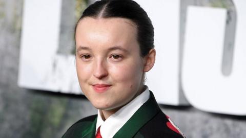Bella Ramsey at the Last of Us premiere wearing a dark green suit and red tie