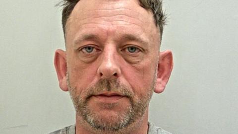 Steven Murphy's mugshot. He has dark short hair, a short salt and pepper beard and blue eyes