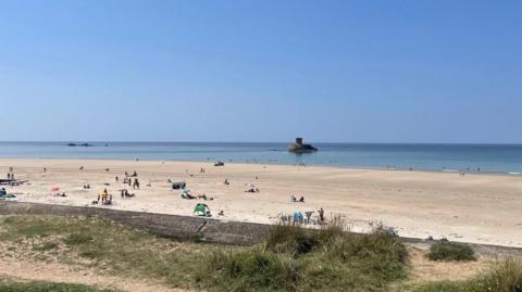 Le Braye beach in Jersey on a sunny day. Dozens of people are on the sand.
