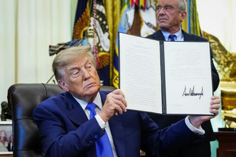 US President Donald Trump holds up an executive order he signed that aims to change childhood vaccine administration