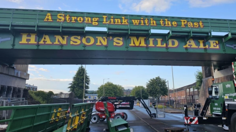 A green metro bridge with the words a strong link with the past and below it Hanson's Mild Ale in gold writing 