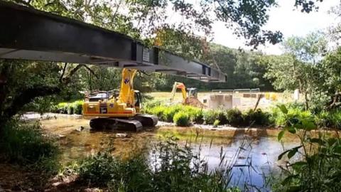 A digger lifting a bridge into place over a river