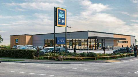 A CGI image of what the new Aldi in Horncastle would look like. There is a car park with cars parked surrounding the store, which is off a main road. The sky is blue with clouds.
