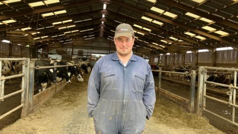 a farmer dressed in overalls standing in a cow barn