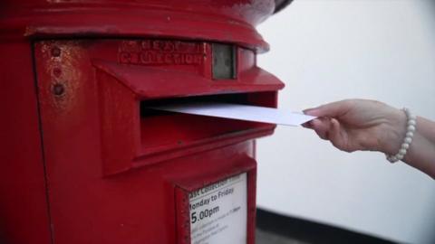 Woman's hand posting a letter into a red post box