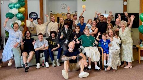 Zane, his family, friends and hospice staff pose for a photo among celebrate his 19th birthday among green, white and gold balloons