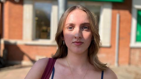 A student in the Leeds suburb of Headingley. She has brown hair and a red brick building is blurred behind her.