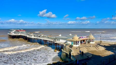 photo of Cromer pier with lots of sunny spells above and with choppy waves beneath