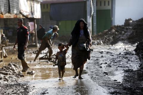 woman holds child by the hand while walking barefoot on a street covered with mud