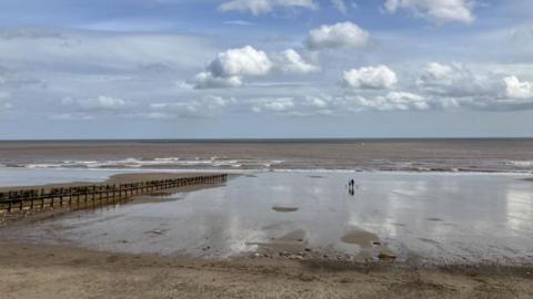 A landscape photo of Hornsea beach with two people walking in the distance