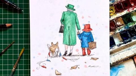 A drawing of the back of Queen Elizabeth II, dressed in a green coat, a green hat and brown shoes, holding a brown bag. She is walking hand in hand with Paddington Bear, wearing a blue coat, a red hat and red wellies, carrying a brown suitcase. A corgi is also walking next to Queen Elizabeth II, with red white and blue bunting draped over it. It is sketched on a white piece of paper and laid on art equipment, including paints and pain brushes.
