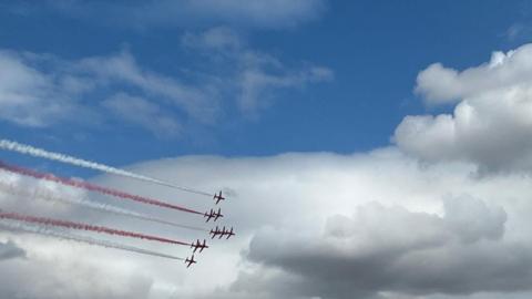Red Arrows flying in formation, with red and white smoke trailing behind