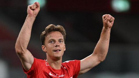 Felix Horn Myhre celebrates a win for SK Brann by putting both arms in the air. He is wearing a red shirt.