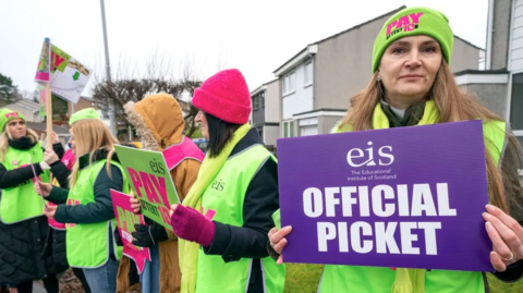 Striking teachers holding placards saying EIS official picket