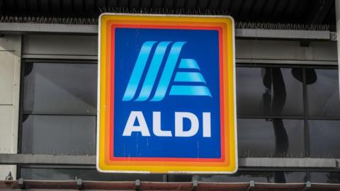 A yellow, orange and red border on a blue rectangular logo with the store name 'Aldi' in the centre