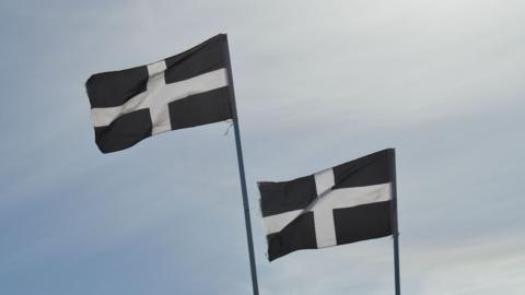 Two Cornwall flags - a white cross on a black background - wave in the air