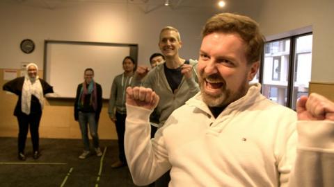 Image of a man cheering in front of a queue of other people