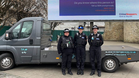 Three female police officers stood next to the grey van, which has a large screen fixed to it.