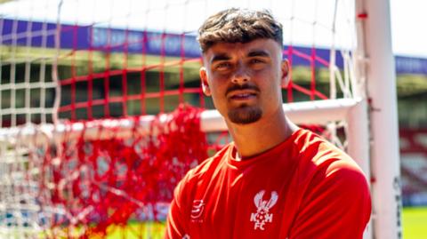 Olly Tipton poses in a Kidderminster training top with the goal behind him