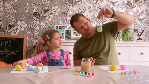 A father and daughter engaging in painting and decorating easter eggs at a table in a living room.