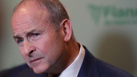 Taoiseach Micheál Martin's face strains and eyebrows furrow, causing his forehead and eyes to wrinkle. He is wearing a dark navy suit jacket and a white shirt. Only his head and a small part of his shoulder are in the frame.   
