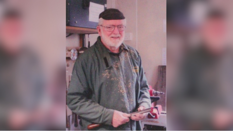 A man holding a tool and standing inside. He looks like he is woodworking.