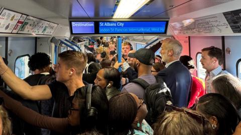 Packed commuter train with large number of people standing in carriage