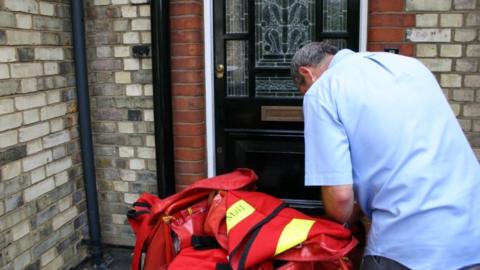 Royal Mail postman with red and yellow sack of items outside a front door