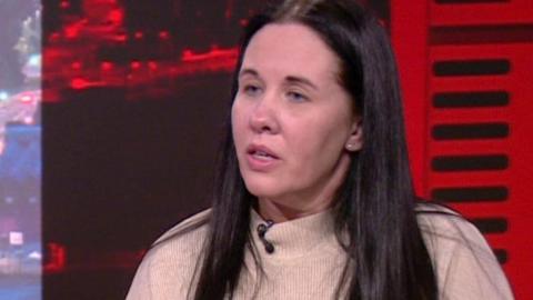 Sharon with long dark hair wearing a cream jumper in the BBC North West Tonight studio.