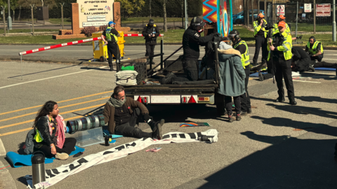 Demonstrators sitting on the floor and attached to a vehicle outside the entrance to RAF Lakenheath. Police officers are also on the scene.