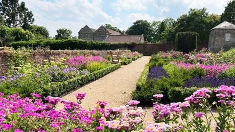 A garden with a gravel path and pink and purple flowers.