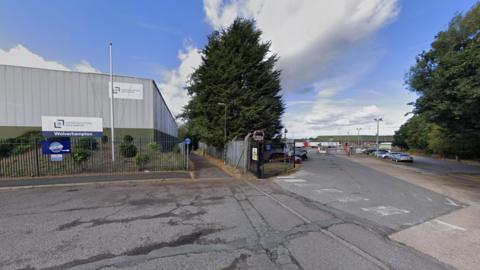 A road in front of a warehouse and car park. 