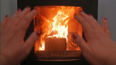 A person warms their hands on a wood-burning stove at a home 