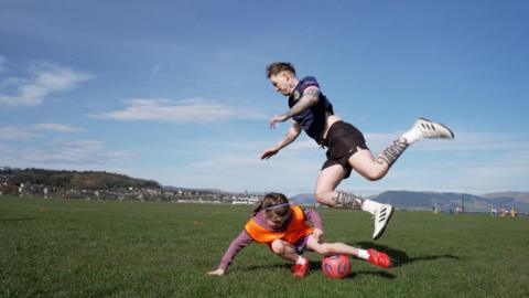 Sgoilear òg a' cluich ball-coise le Cailean Stone