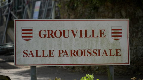 A sign outside of a building which says 'GROUVILLE / SALLE PAROISSIALE' which translates to Parish Hall in French.