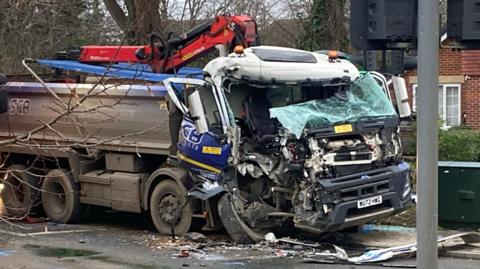 A smashed up lorry on the side of a road. There is debris all around it.