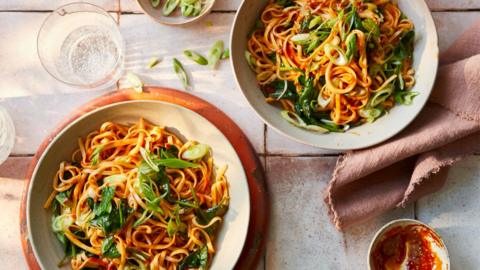 Two bowls filled with noodles covered in a red coloured sauce, topped with spring onions sliced thinkly.