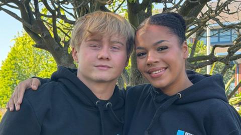 Two dancers from the LMA group wearing dark hoodies and sat outside smiling, Michael and Rose