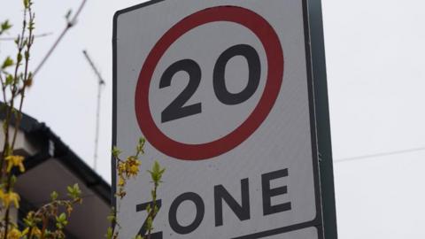 A 20mph zone symbol on a white road sign