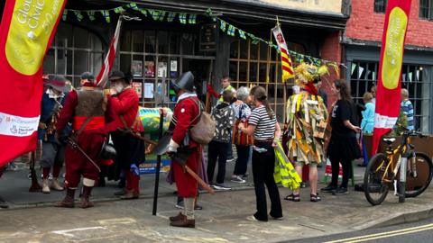 A group of people dressed in historical costumes stand outside of a shop in Gloucester.