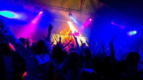 A generic image of a nightclub with a DJ set in the background and dancers in the foreground