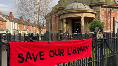 The Meadows Library in Nottingham with a 'Save our Library' banner hanging on the gate outside. 