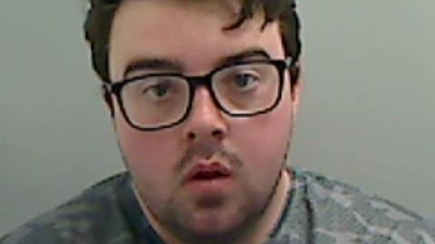 Mugshot of Callum Wray. He has a large round face, with black-framed glasses and short black hair.